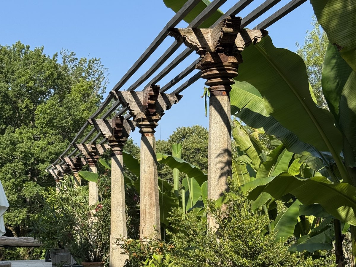 La pergola de poutres portée par ses colonnes de granit, dans les bananiers
