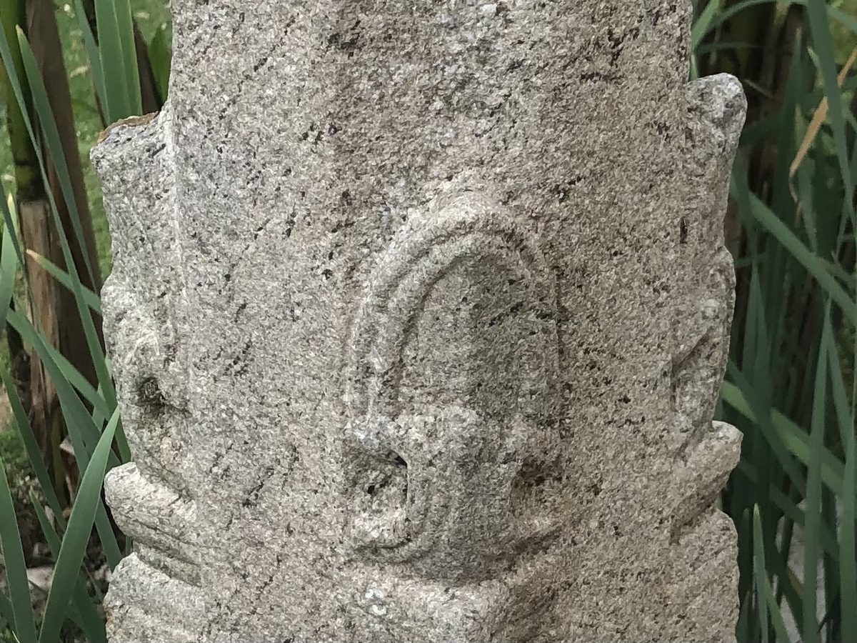 Une colonne de granit sculptée, dressée dans les herbes du jardin